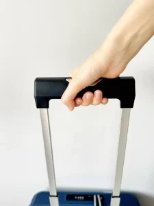 Workers testing the ergonomic telescopic luggage handle with textured grip. The handle features a 6063 aluminum bar with a center distance of 135 cm, a spring-loaded height adjustment button, and an industrial-grade dust-proof locking device.